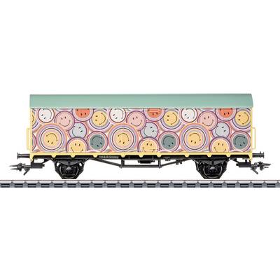 Ein Zugwagen mit bunten Smileys und kreisförmigen Mustern. Das Dach ist grün, und der Wagen steht auf einem Gleis, von der Seite betrachtet.