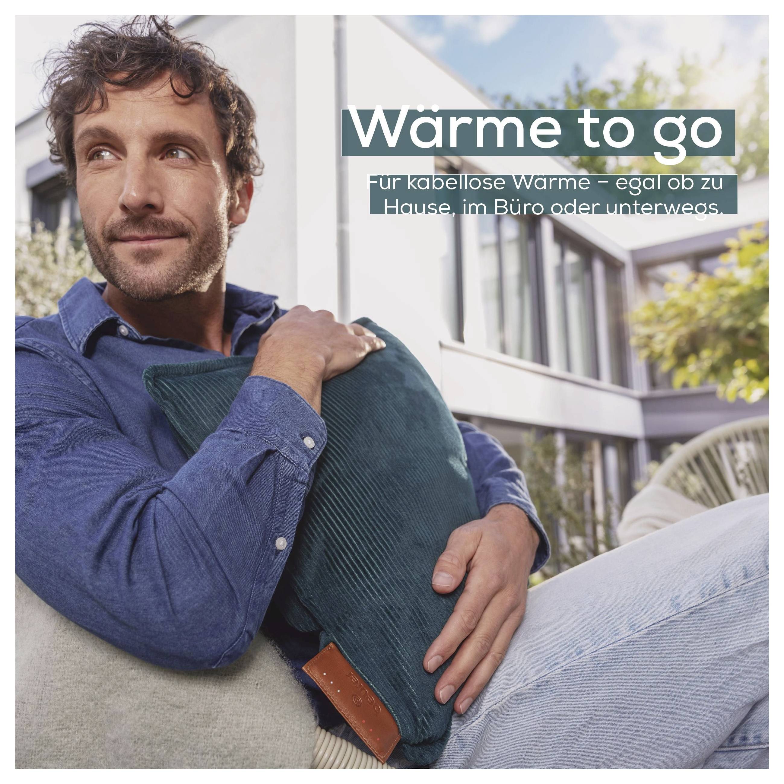Ein Mann sitzt im Freien mit einem türkisfarbenen Kissen. Der Text auf Deutsch lautet „Wärme to go" und erwähnt tragbare Wärme für zu Hause, Büro oder zum Reisen.