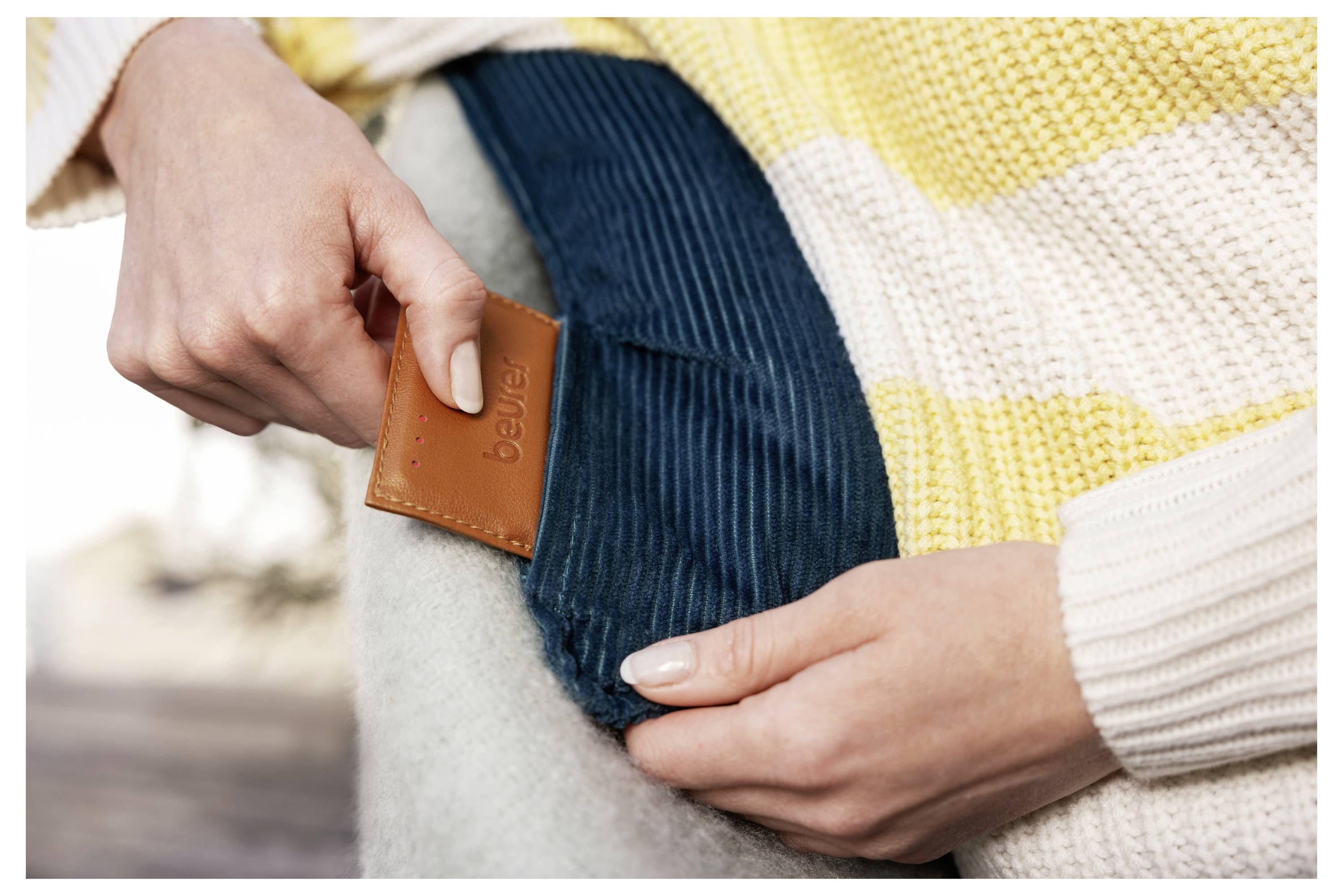 Eine Person legt eine braune Lederkarte mit der Bezeichnung „bewear" in eine blaue Tasche. Sie trägt einen gelb-weiß gestreiften Pullover.