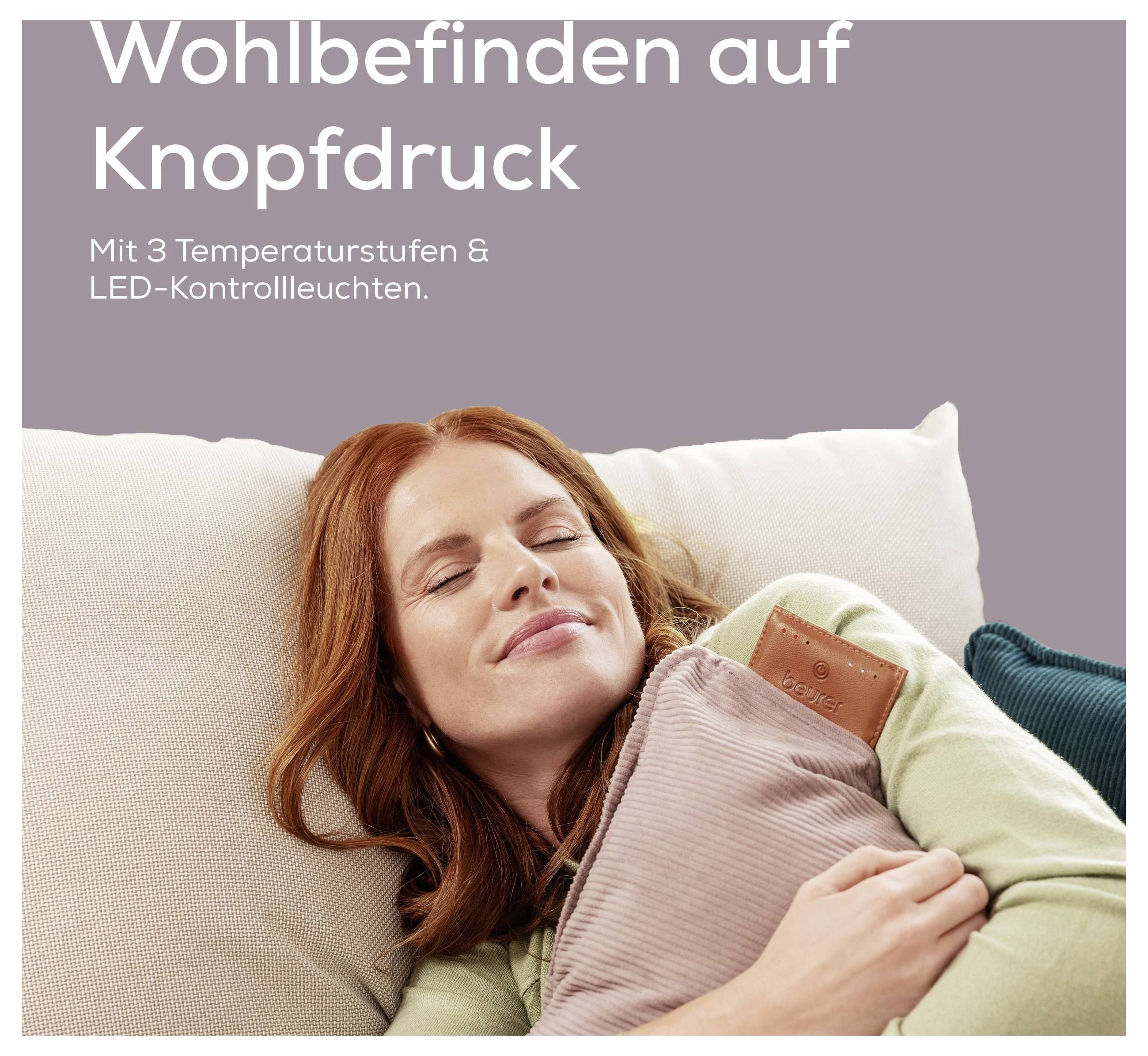 Eine Frau entspannt sich auf einem Sofa und hält ein Wärmekissen. Der Text lautet: „Wohlbefinden auf Knopfdruck. Mit 3 Temperaturstufen & LED-Kontrollleuchten."