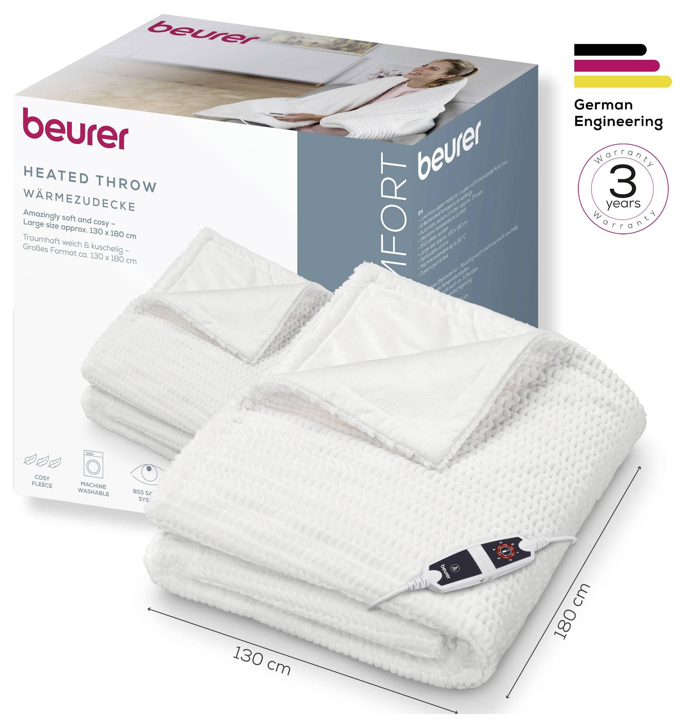 Eine weiße beheizte Wurfdecke mit Bedienfeld wird neben ihrer Verpackung angezeigt, beschriftet mit „beurer", „Wärmedecke" und „130 x 180 cm". Deutsche Ingenieurskunst mit einer 3-jährigen Garantie wird hervorgehoben.