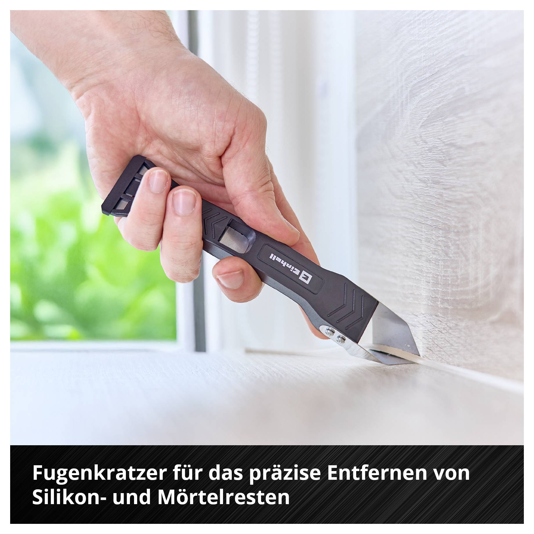 'Hand hält Fugenkratzer und entfernt Silikon- und Mörtelreste von einer Kante.'