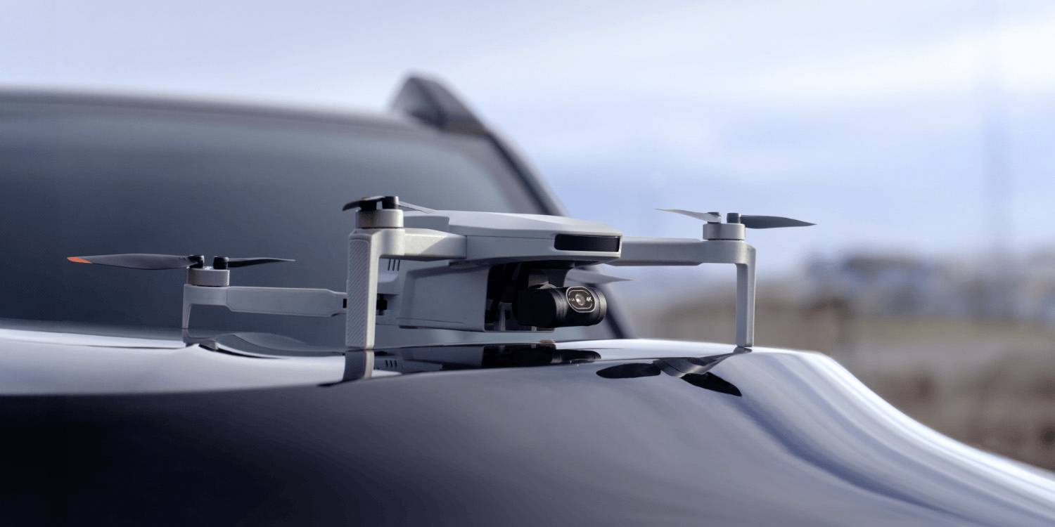 Eine kompakte Drohne ruht auf einer Motorhaube eines Autos, bereit zum Flug, und spiegelt moderne Technologie und Mobilität in einer Außenumgebung wider.