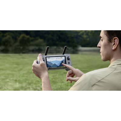 Eine Person, die eine Drohnensteuerung hält, konzentriert sich auf den Bildschirm, der einen Live-Feed einer Berglandschaft anzeigt, was auf die Verwendung im Freien hindeutet.