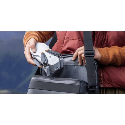 Eine Person, die eine kompakte Drohne in eine graue Tasche legt; trägt eine rote Jacke und einen orangefarbenen Pullover.