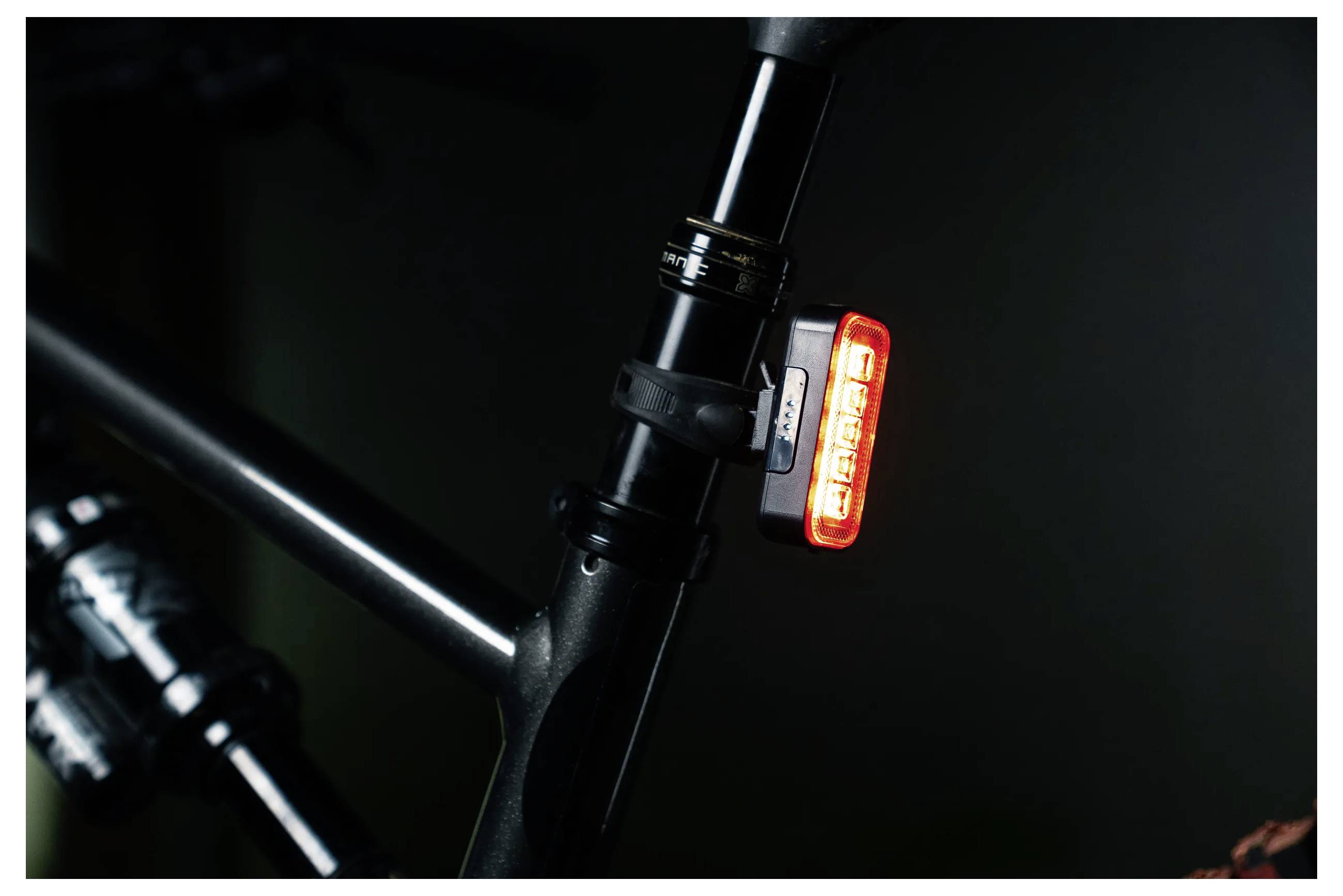 Eine Fahrrad-Sattelstütze mit einem roten LED-Rücklicht, befestigt mit einem Gummiband, das in einer schwach beleuchteten Umgebung hell leuchtet.