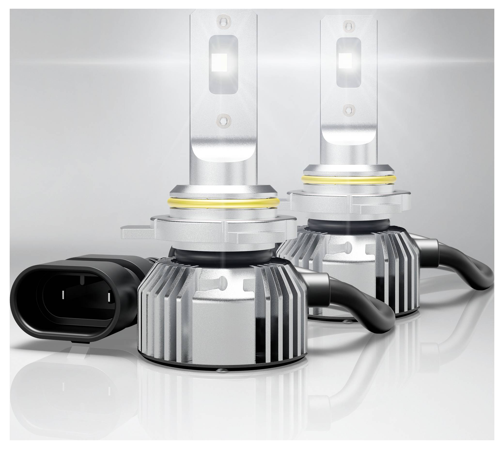 Zwei LED-Scheinwerferlampen mit Kühlrippen und angebrachten Stromsteckern sind auf einer reflektierenden Oberfläche positioniert, die ihre metallische Oberfläche hervorhebt.