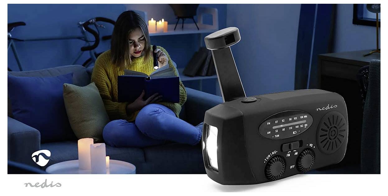 Eine Person liest bei Kerzenlicht zu Hause ein Buch. Im Vordergrund ist ein tragbares Radio mit analoger Abstimmung und eine Taschenlampe sichtbar.