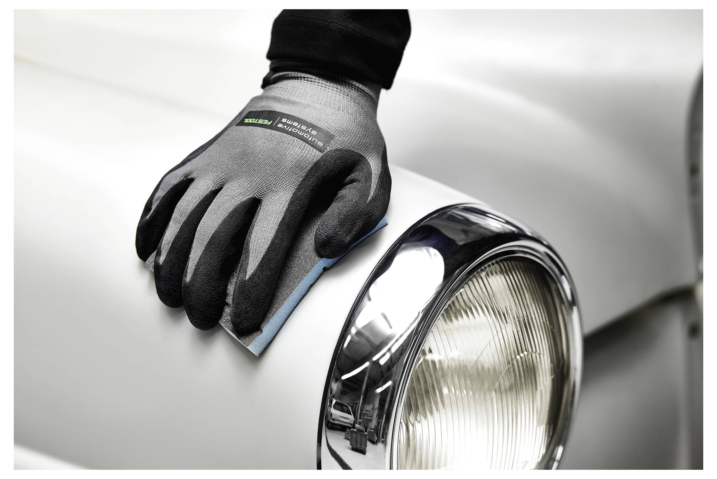 Eine behandschuhte Hand poliert die weiße Außenseite eines Vintage-Autos in der Nähe des Scheinwerfers und hebt den glänzenden und gepflegten Zustand des Fahrzeugs hervor.
