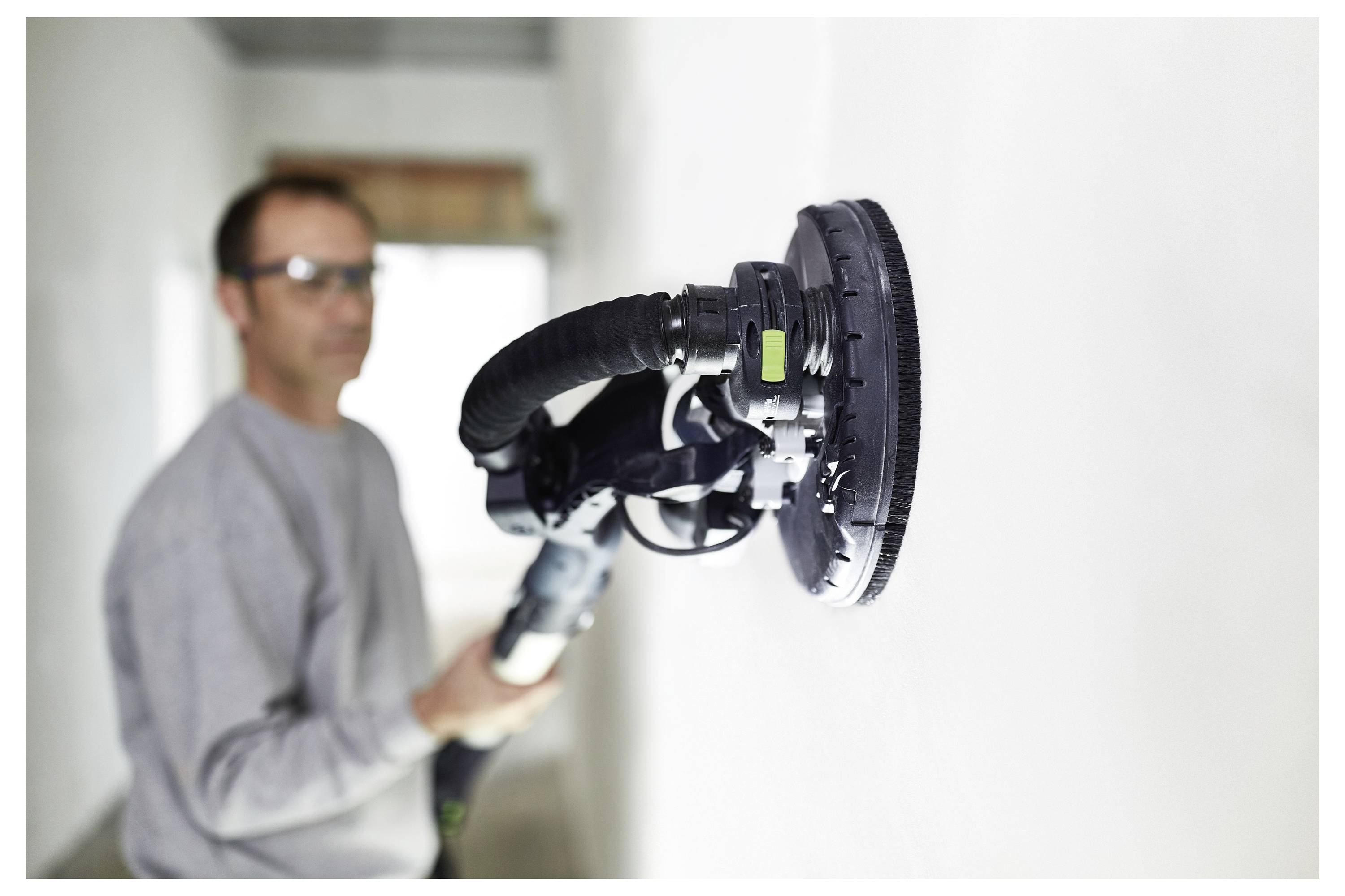 Eine Person verwendet einen elektrischen Schleiffer an einer weißen Wand und konzentriert sich auf die Glättung der Oberfläche.