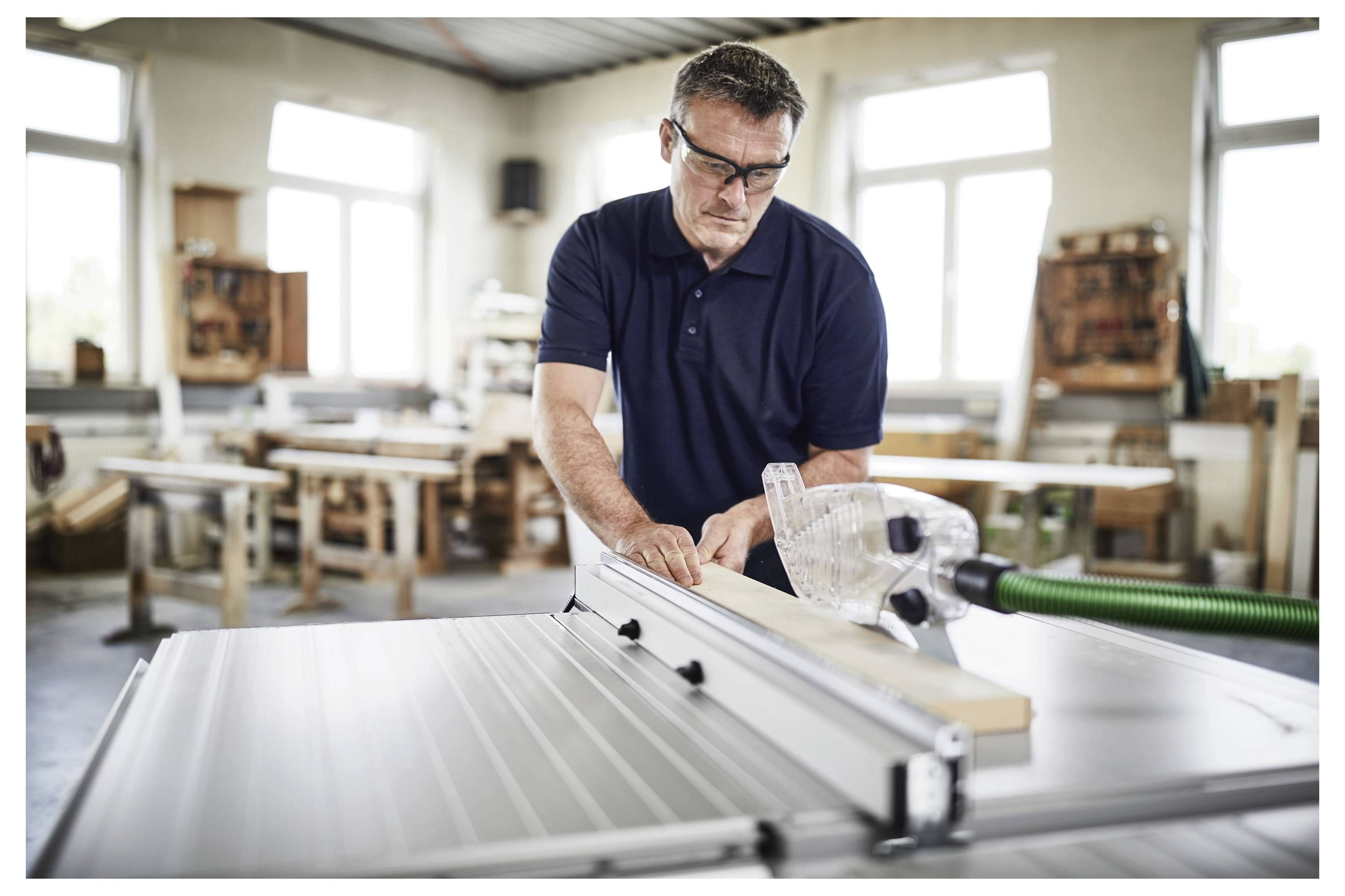 Eine Person verwendet eine Festool-Kreissäge, um ein Holzbrett, das auf einem Sägebock positioniert ist, in einer Werkstattumgebung zu schneiden.