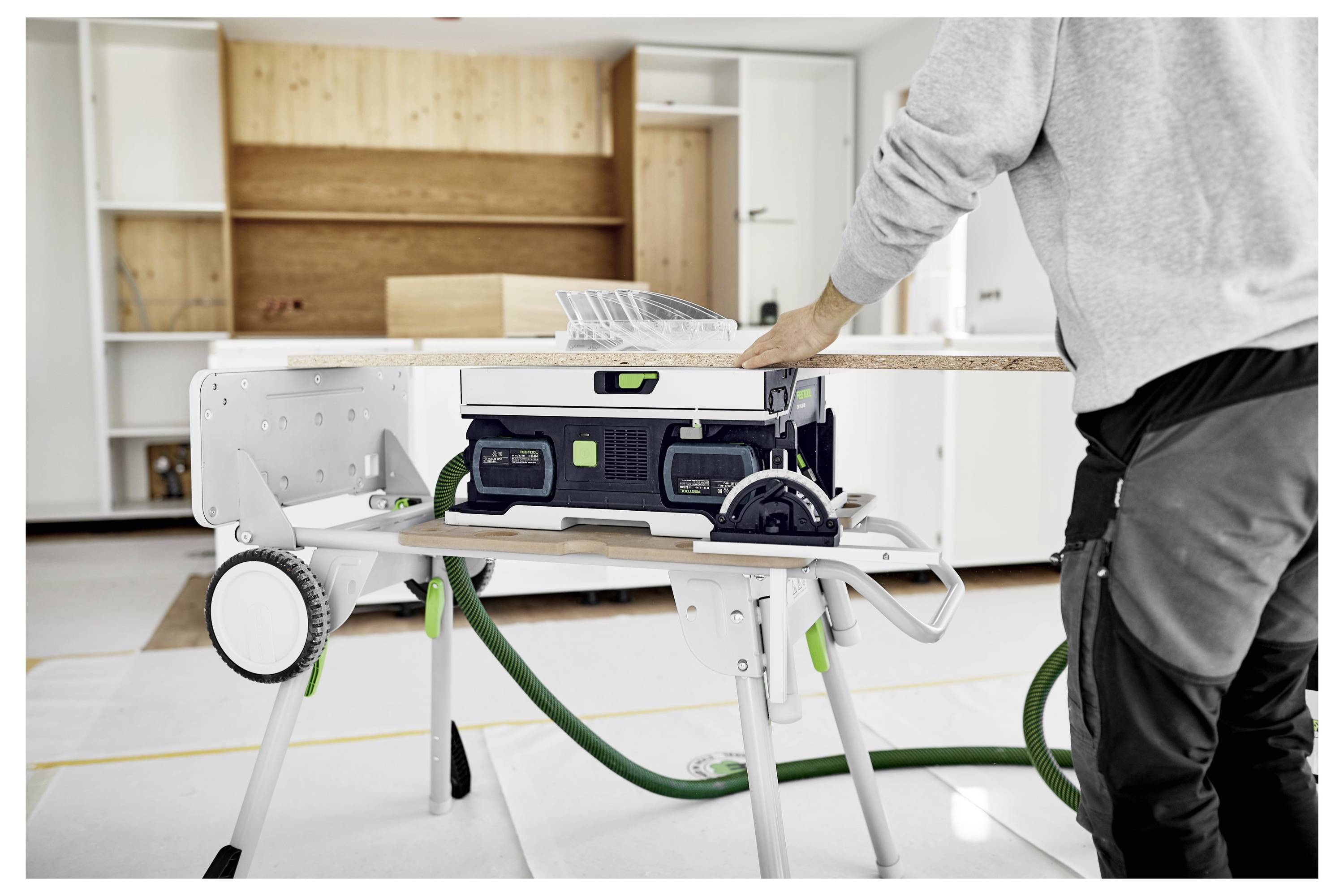 Eine Person verwendet eine Säge auf einem Holzbrett, verbunden mit einem Festool-Staubabsauger, wobei die effiziente Arbeitsplatzvorbereitung und Staubabsaugung hervorgehoben wird.