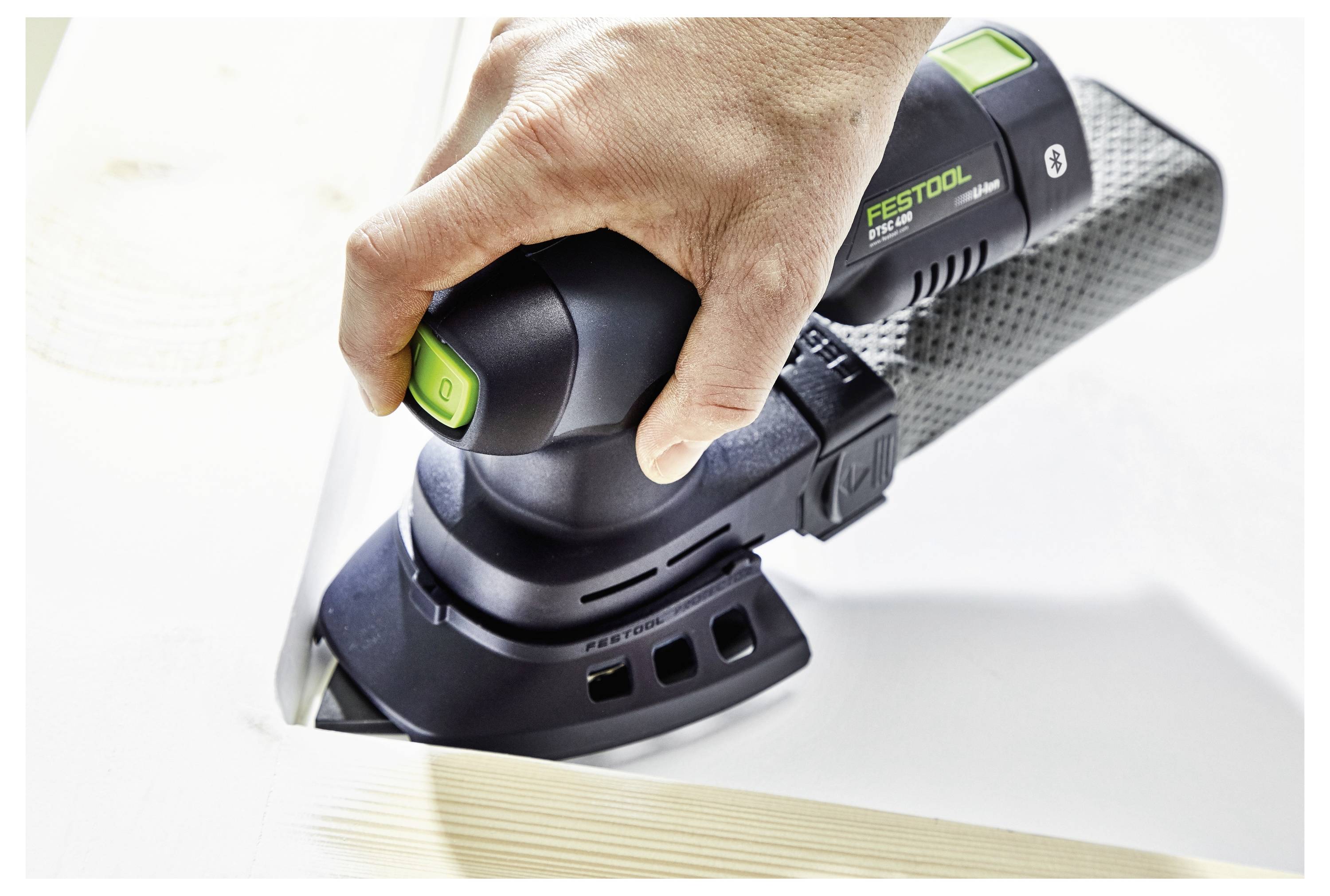 Eine Hand benutzt einen Elektroschleiffer, um die Kante einer Holzoberfläche zu glätten. Das Werkzeug ist ein Festool-Modell, das sein ergonomisches Design hervorhebt.