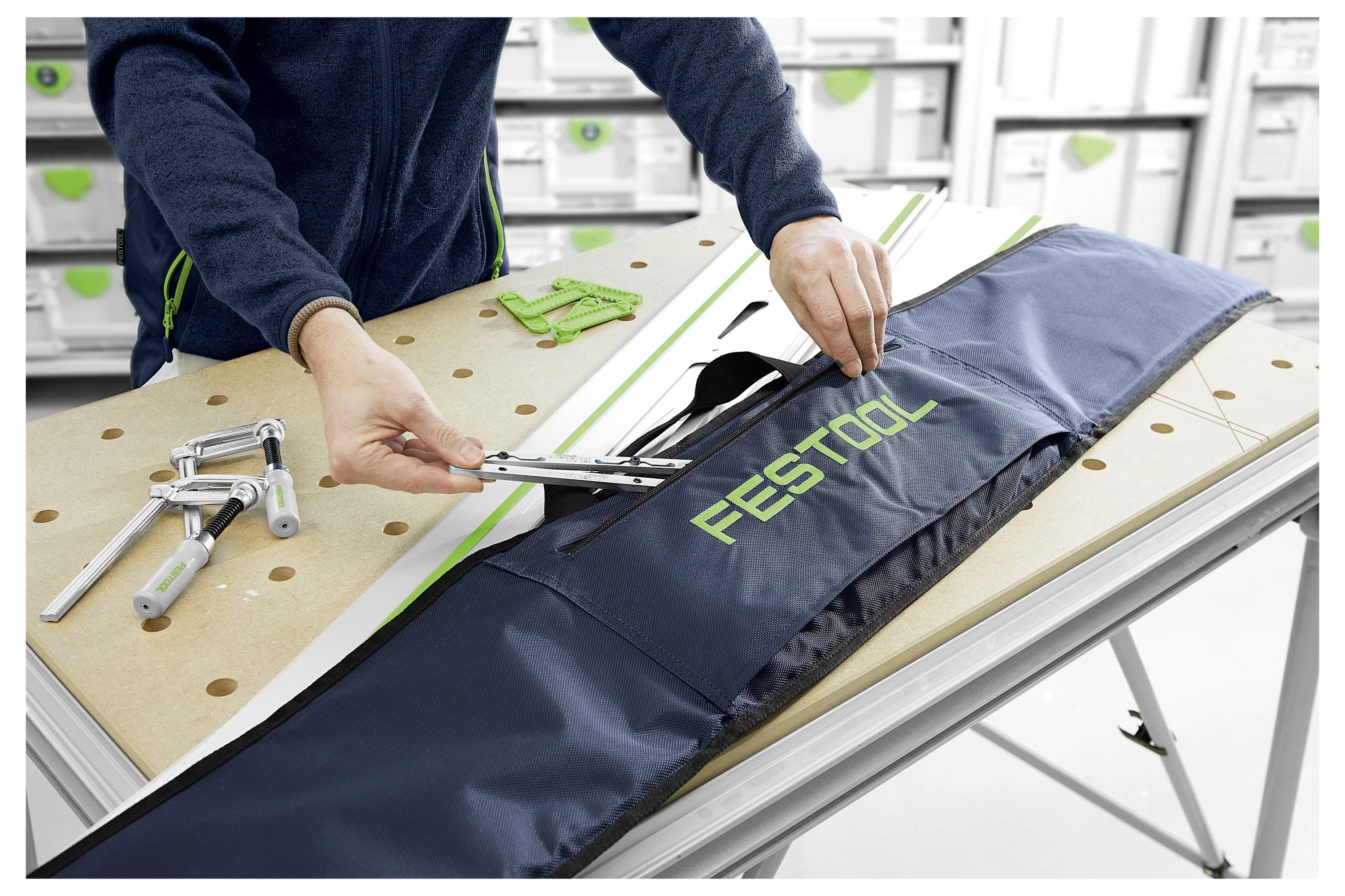 Eine Person legt Werkzeuge in eine Festool-Werkzeugtasche auf einer Werkbank. Der Hintergrund zeigt Regale mit Lagerkisten.