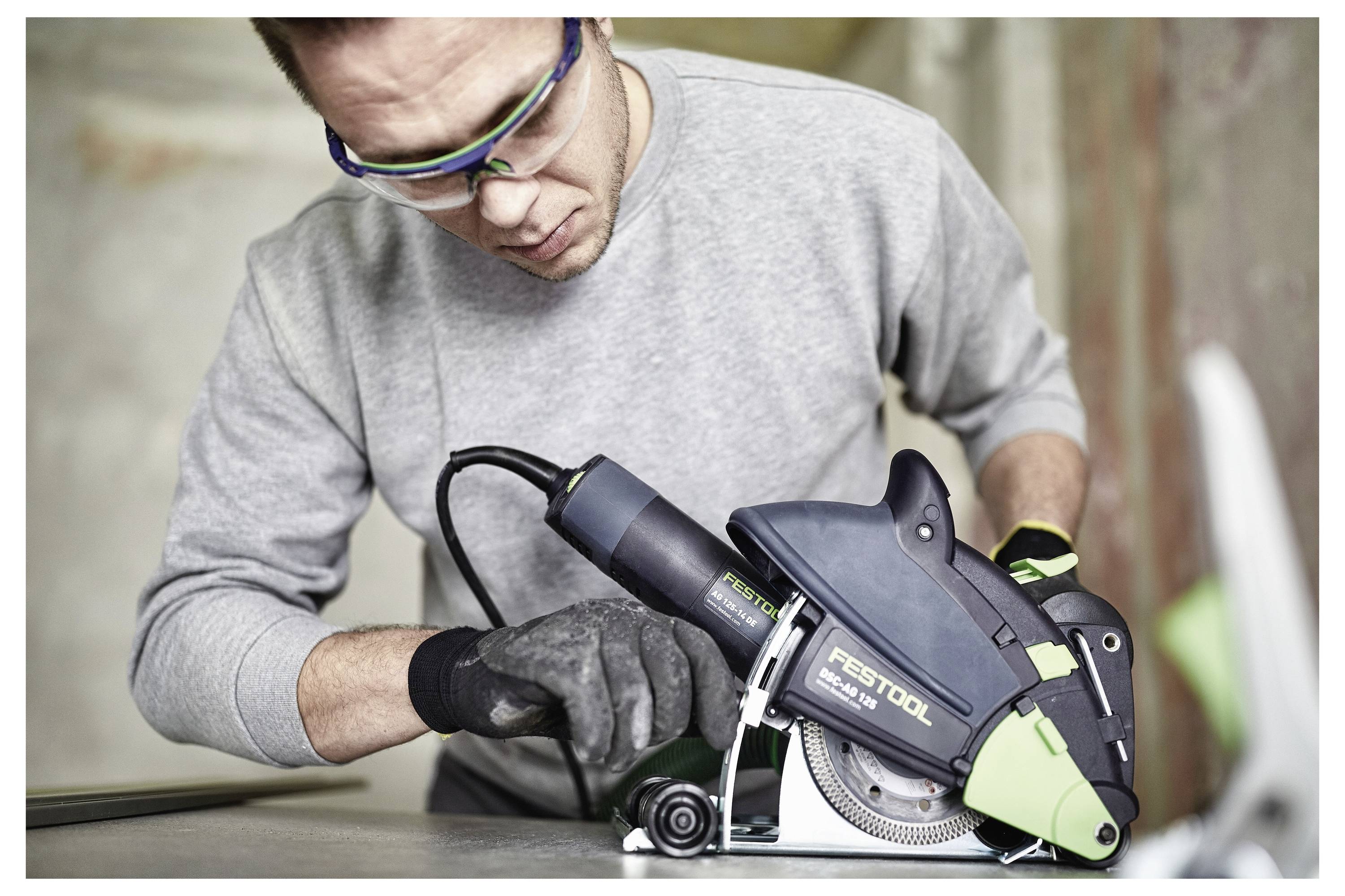 Eine Person, die Schutzbrille und Handschuhe trägt, bedient eine Festool-Säge und konzentriert sich intensiv darauf, was auf Präzision und Sicherheit bei Bauarbeiten hindeutet.