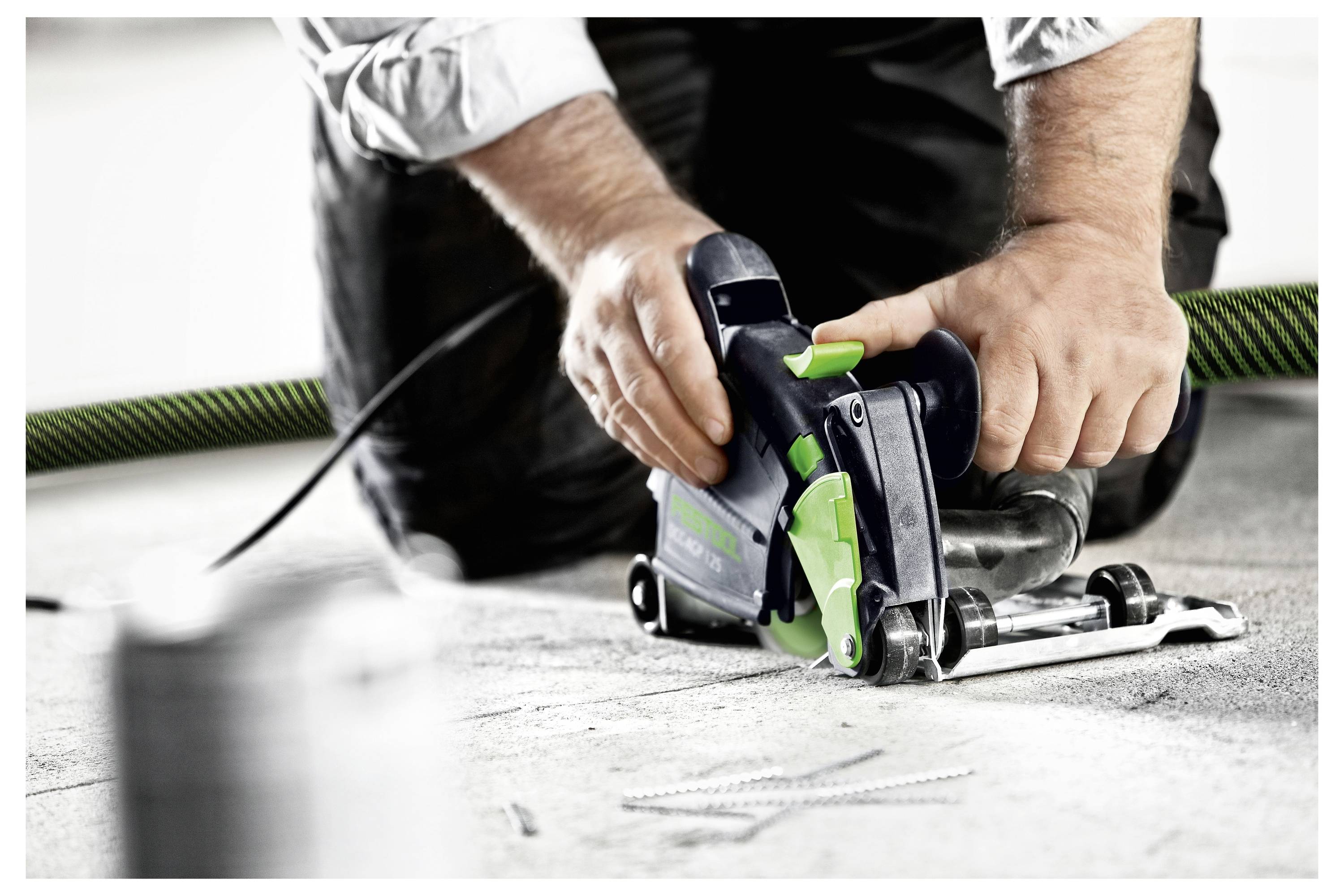 Eine Nahaufnahme eines Elektrowerkzeugs mit einer kreisförmigen Schneideklinge, die die Kante einer Holzoberfläche trimmt. Das Werkzeug verfügt über einen grünen Griff.