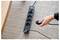 Die Hand einer Person steckt ein Kabel in eine schwarze Steckdosenleiste mit vier Anschlüssen, die auf einem strukturierten Teppich platziert ist.