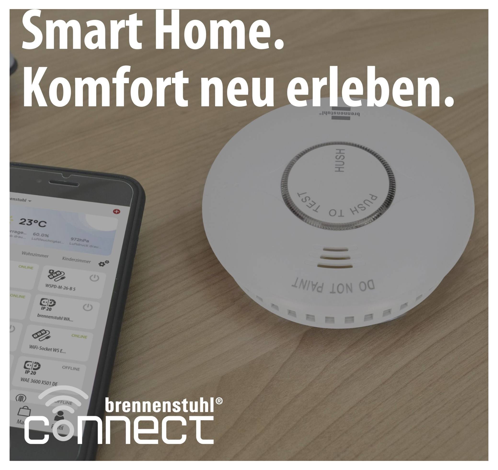 Werbeabbildung für Smart-Home: Smartphone-App steuert ein Brennenstuhl-connect-Gerät neben einem Rauchmelder auf Holztisch, mit Text 'Smart Home. Komfort neu erleben.'<br>
