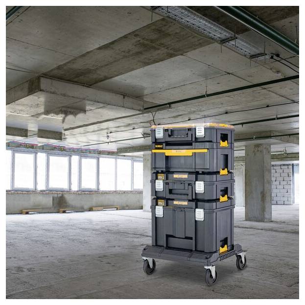 Ein Stapel von vier Industrie-Lagerkästen auf einem Handwagen mit Rädern in einem unvollendeten Betonraum mit freiliegenden Decken und großen Fenstern.