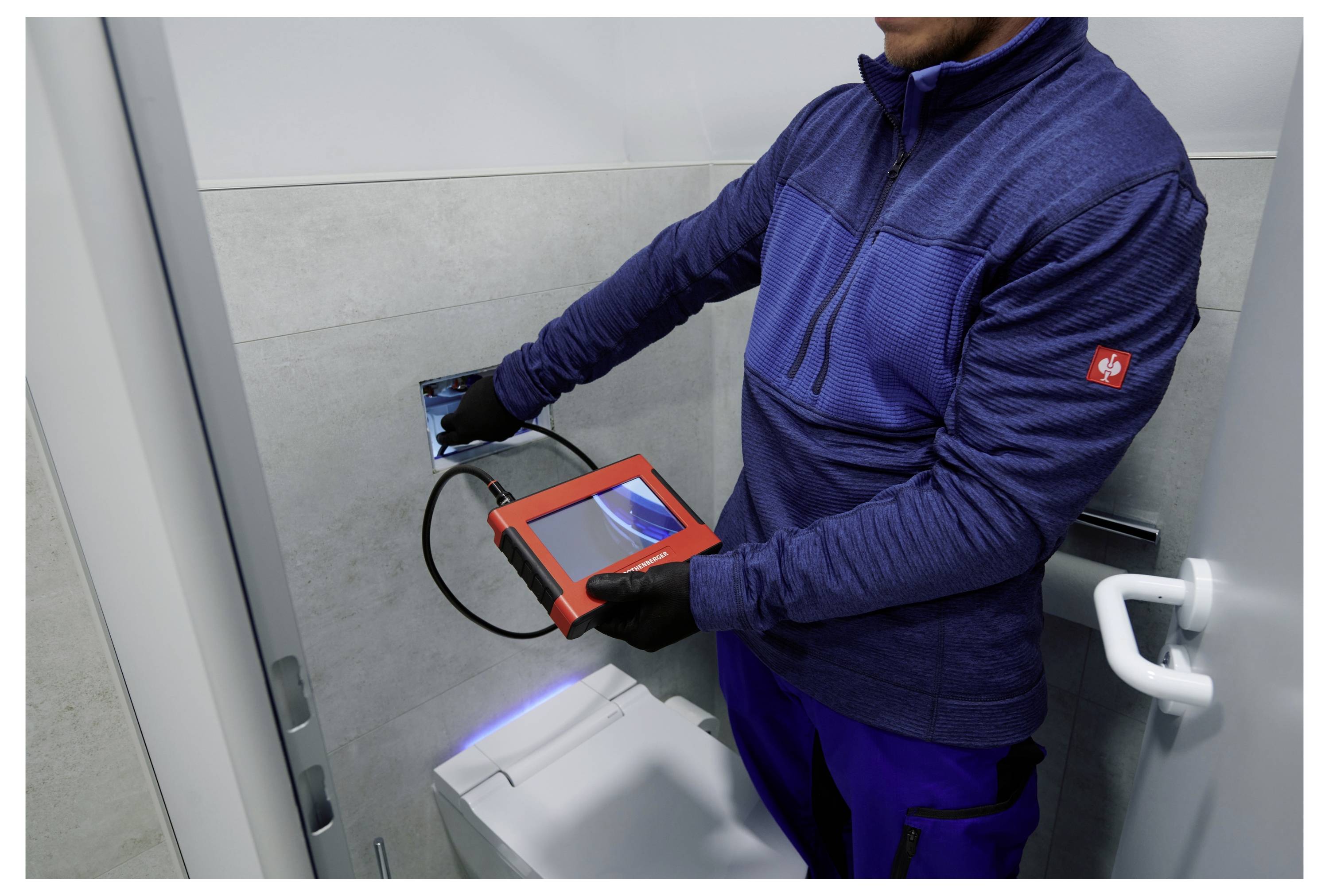 Ein Techniker in blauer Uniform nutzt ein Kamerawerkzeug, um das Innere eines Toilettenspülkastens zu inspizieren und auf Wartungsprobleme zu prüfen.