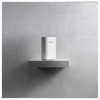 Ein weißes Gerät mit der Aufschrift „devolo", das auf einem minimalistischen Regal vor einer grau strukturierten Wand platziert ist.