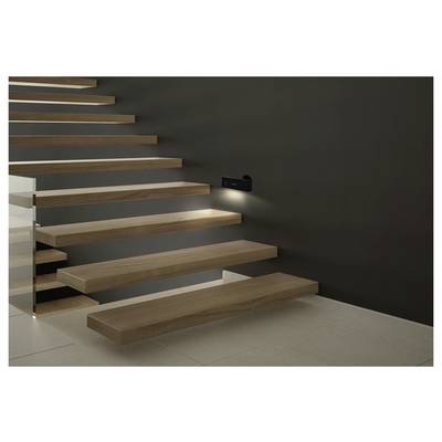 Moderne freischwebende Holztreppe an einer dunklen Wand, beleuchtet durch eine kleine Wandleuchte, mit offenen Stufen und Glasgeländer an der Seite.