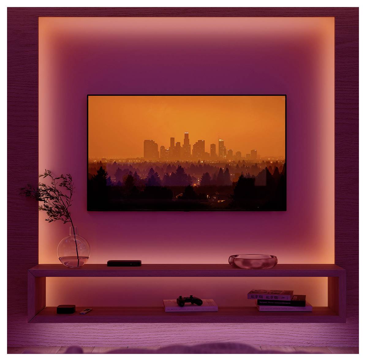 Fernseher an der Wand montiert, zeigt eine in Orangetönen gehaltene Stadtlandschaft, umgeben von rosa Umgebungslicht. Regal darunter mit Dekoration und Elektronik.