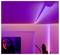 Ein Zimmer mit violett getönter LED-Beleuchtung an Decke und Wänden; ein Fernseher, der im Hintergrund einen Teil eines Gesichts zeigt.
