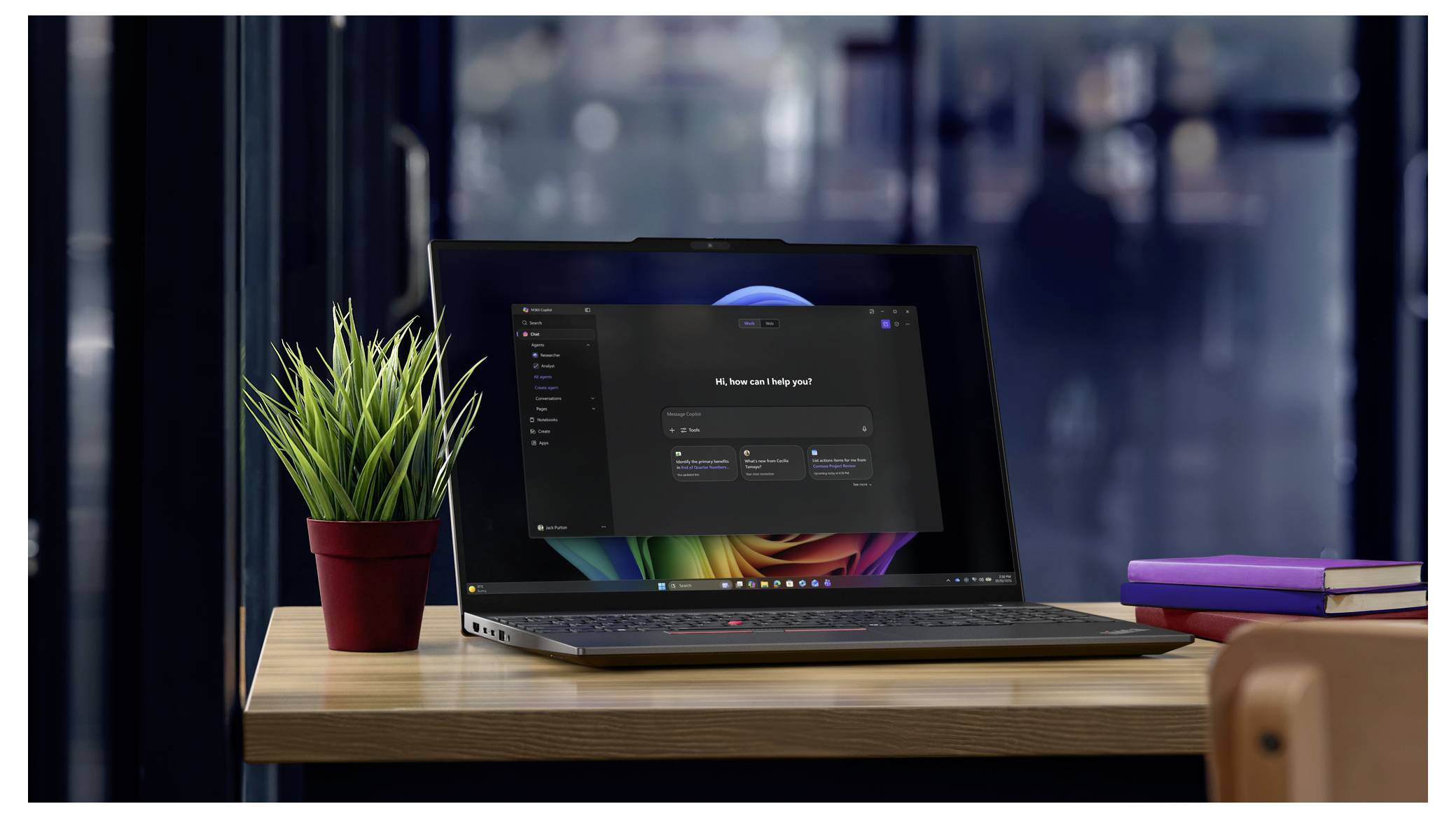 Ein Laptop auf einem Holztisch mit KI-Assistent-Oberfläche, daneben eine kleine Topfpflanze und gestapelte Bücher, in einer Büroumgebung.