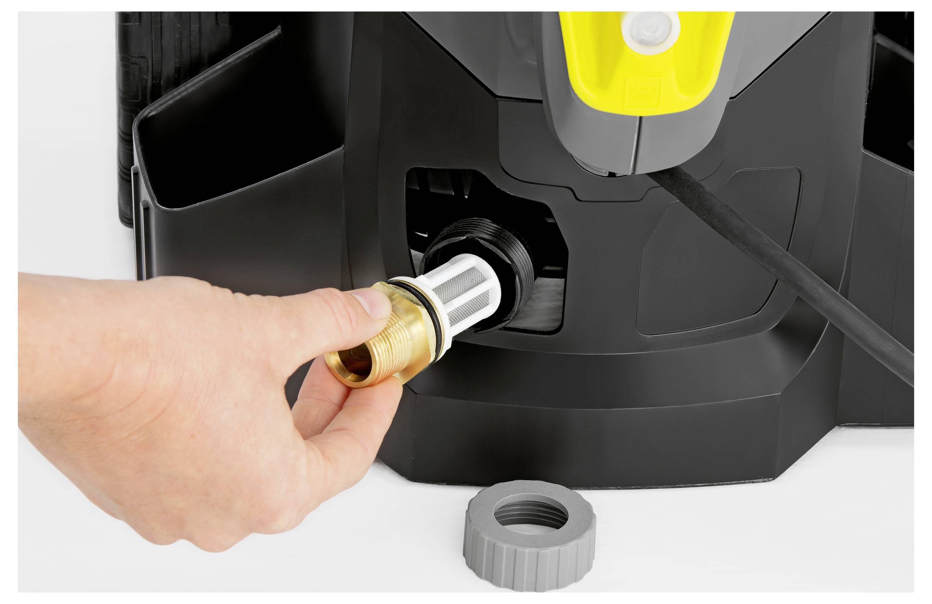 Eine Hand führt einen Schlauchanschluss in ein Hochdruckreinigungsgerät ein und zeigt dabei den Verbindungsprozess. Eine graue Düse sitzt in der Nähe auf dem Boden.