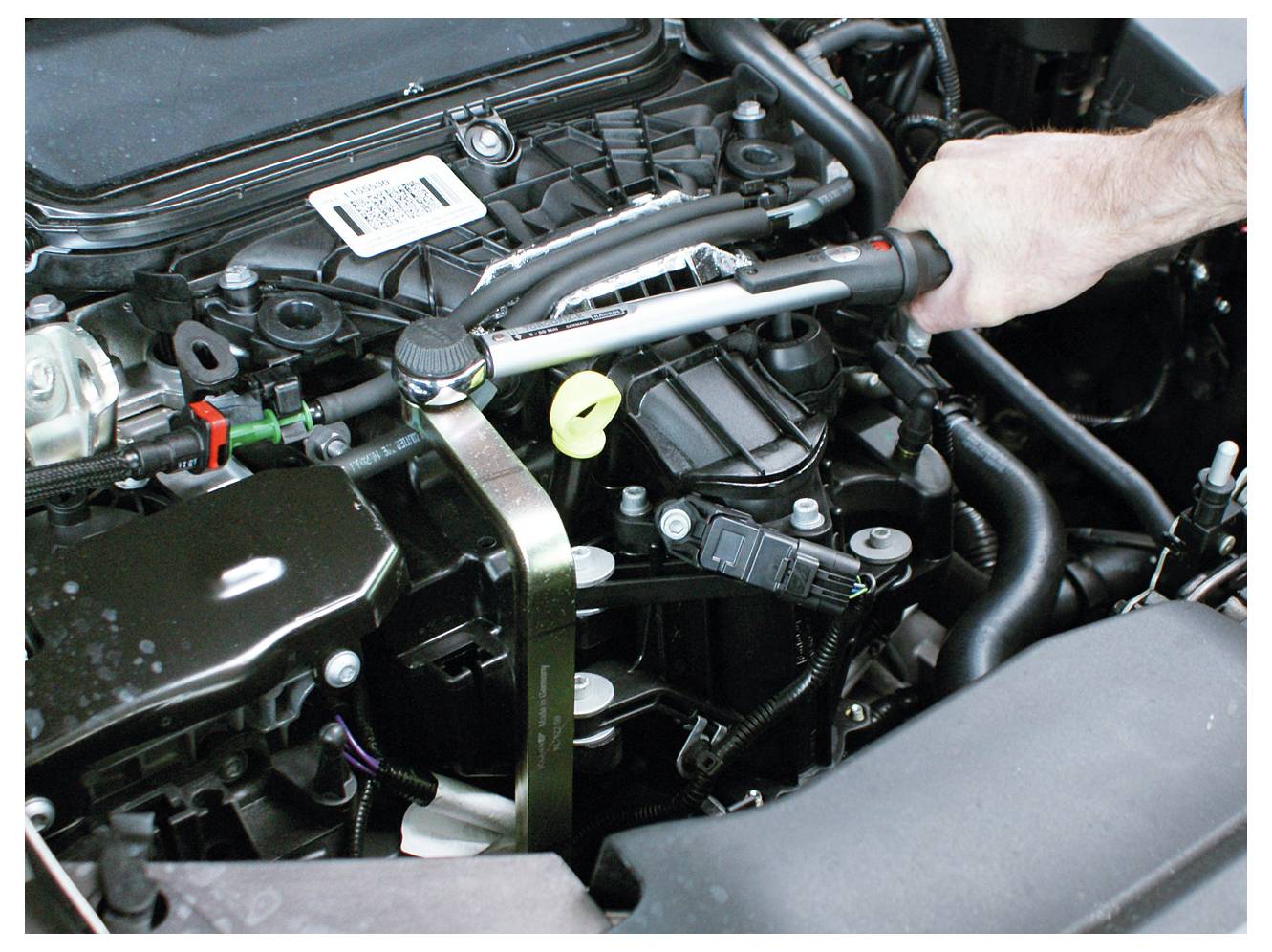 Eine Person verwendet einen Drehmomentschlüssel, um einen Bolzen in einem Automotor festzuziehen und konzentriert sich dabei auf Präzision während einer Wartungsaufgabe.