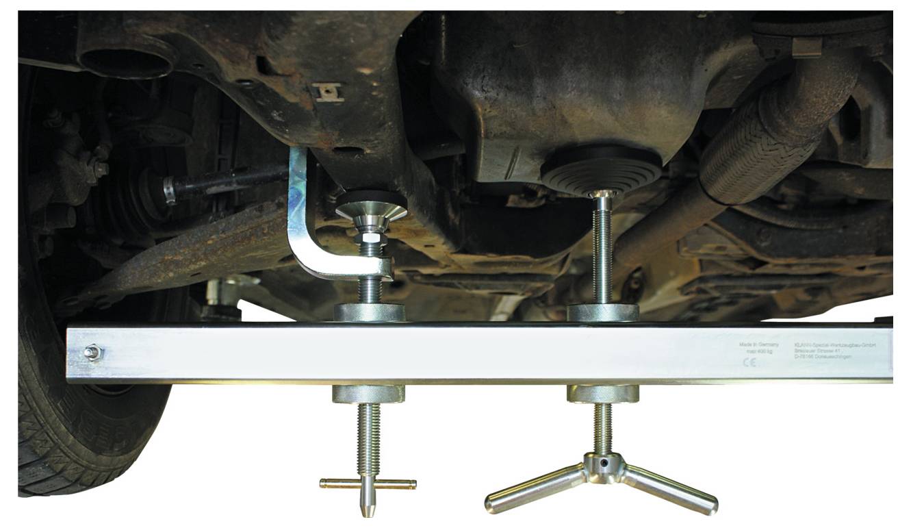 "Unterfahrschutz-Stützwerkzeug", Metallstange mit verstellbaren Spannvorrichtungen zur Stabilisierung der Fahrzeugbodengruppe während der Wartung, mit Betonung auf Sicherheit und Unterstützung.