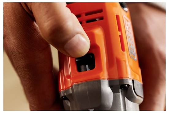 Eine Hand, die ein orangefarbenes Elektrowerkzeug hält, wobei der Fokus auf dem Auslösemechanismus liegt. Das Werkzeug scheint für Bohr- oder Befestigungsaufgaben ausgelegt zu sein.