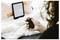 Eine Person, die eine kleine schwarze kabellose Präsenter-Fernbedienung hält, sitzt auf einer flauschigen weißen Oberfläche. Ein E-Reader zeigt Text im Hintergrund an.