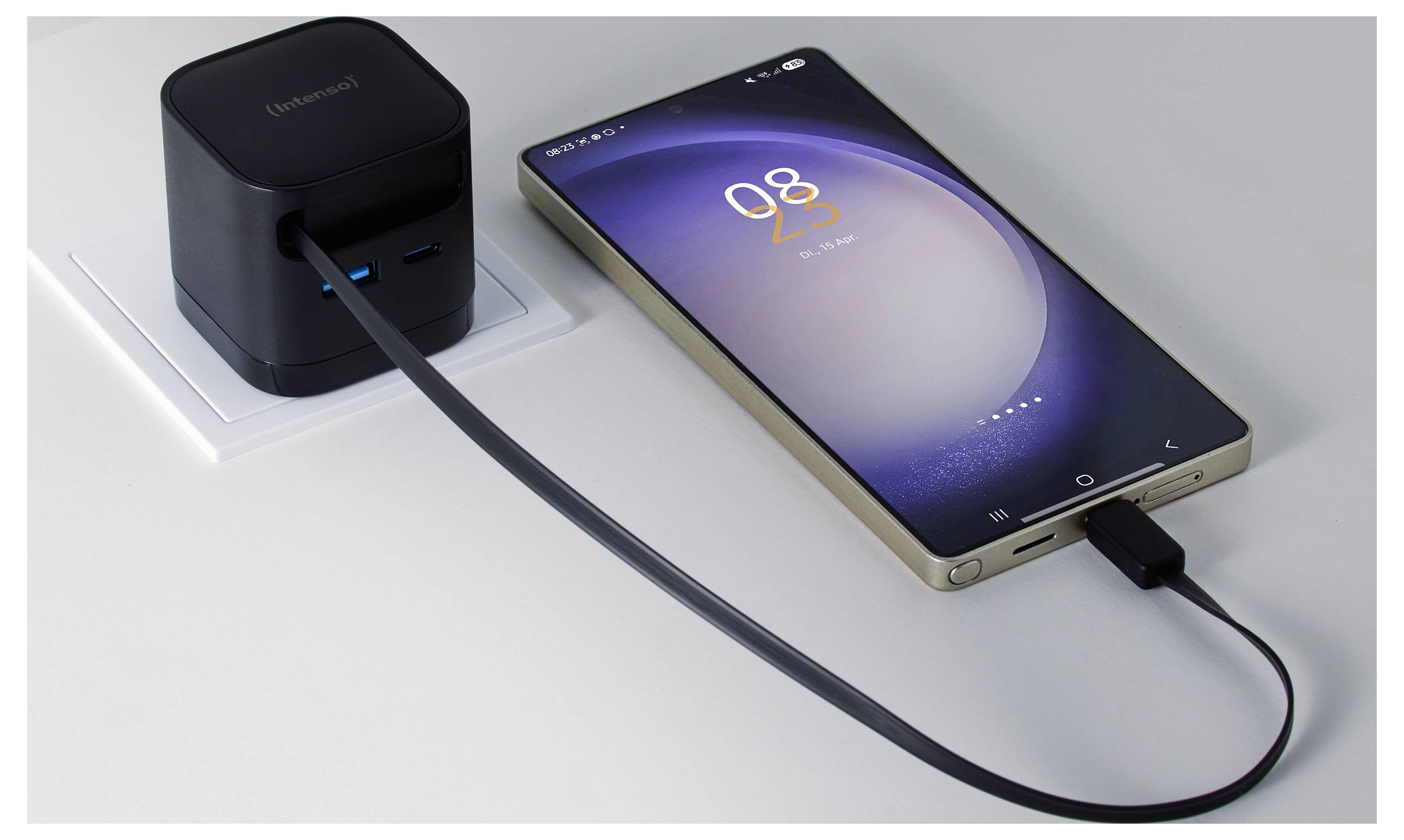 Ein Smartphone lädt auf einer weißen Oberfläche mit einem schwarzen Ladegerät, das an eine Steckdose angeschlossen ist. Das Telefon zeigt '08 23' auf dem Bildschirm an.