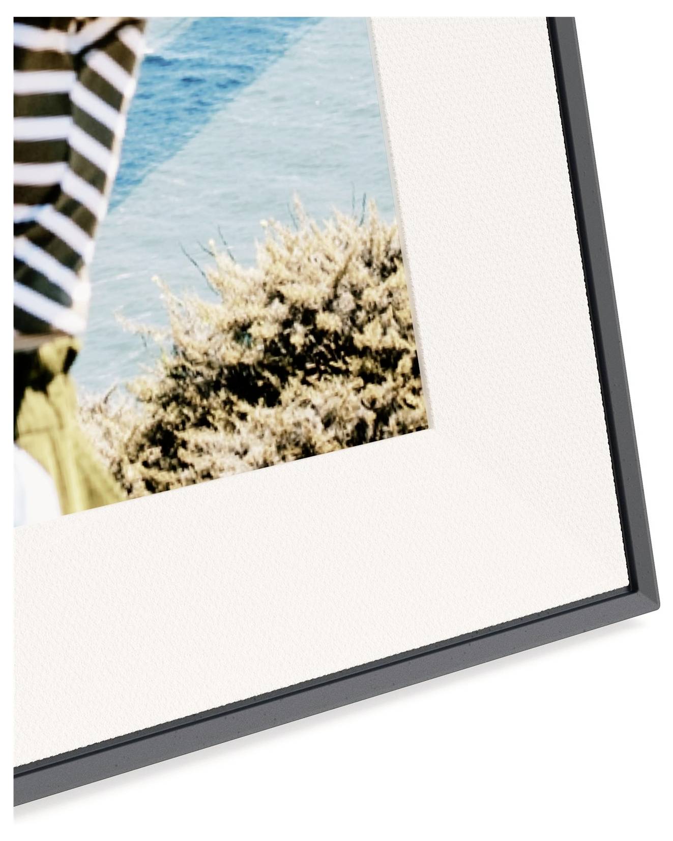 Eine Nahaufnahme einer Fotorahmen-Ecke, die einen Teil der gestreiften Kleidung einer Person und eine Küstenszene mit Vegetation und blauem Wasser zeigt.
