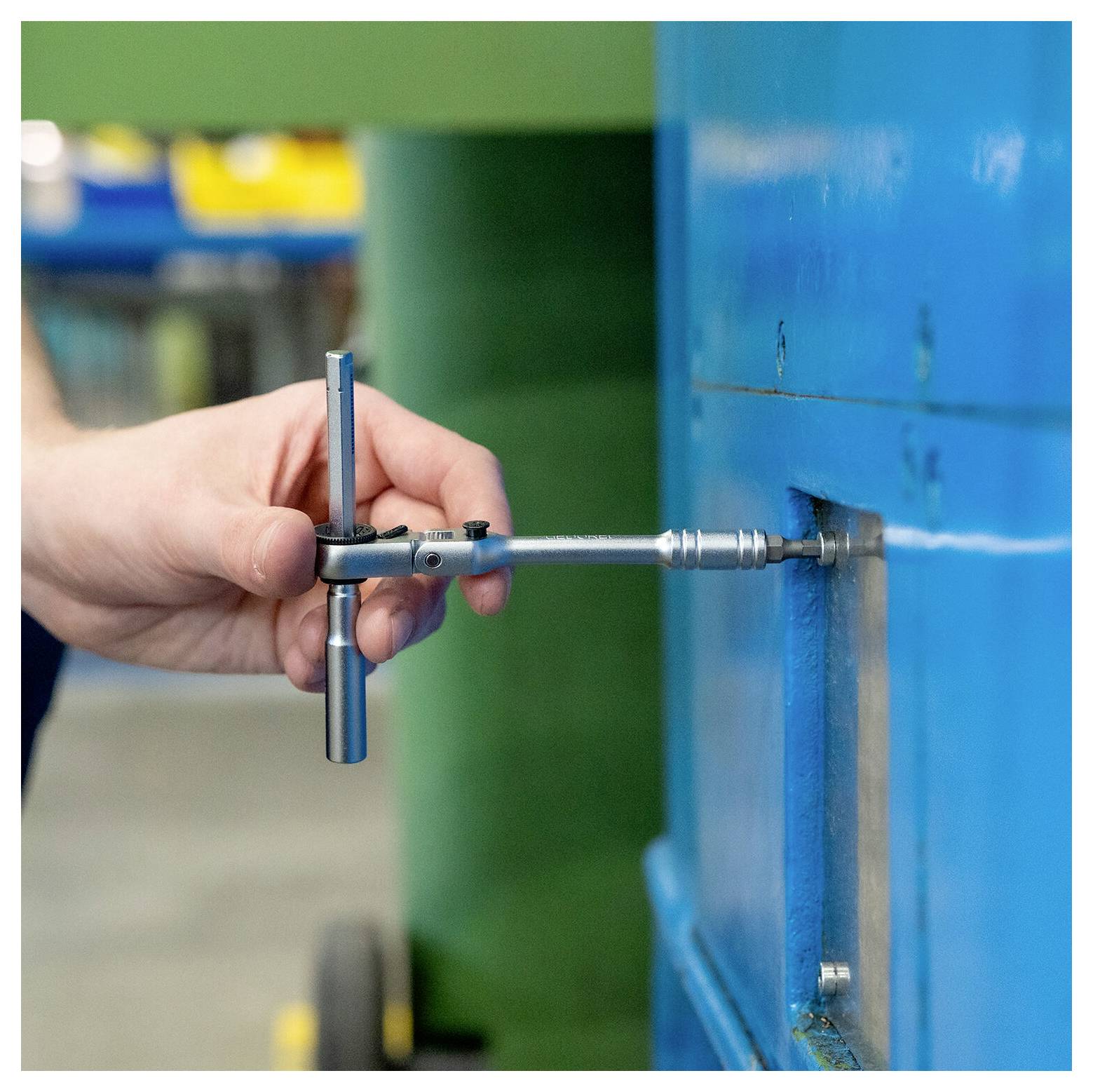 Eine Hand benutzt einen T-Griff-Schraubenschlüssel, um eine Schraube an einer blauen Metallmaschine oder einem Metallpaneel anzuziehen oder zu lockern.