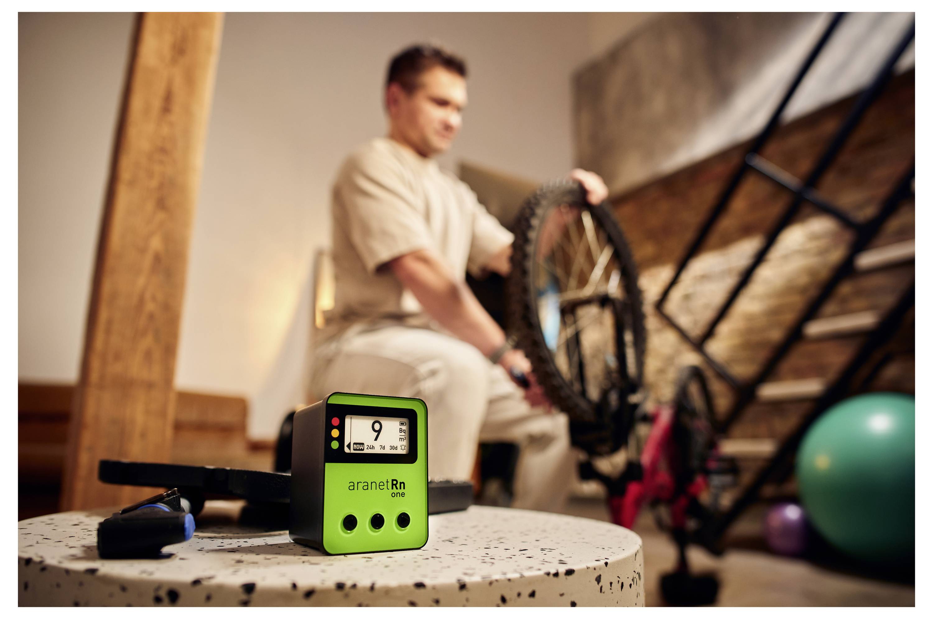 Ein Mann repariert ein Fahrrad im Hintergrund, während im Vordergrund ein grünes digitales Gerät mit der Anzeige '9' auf einem Tisch steht.