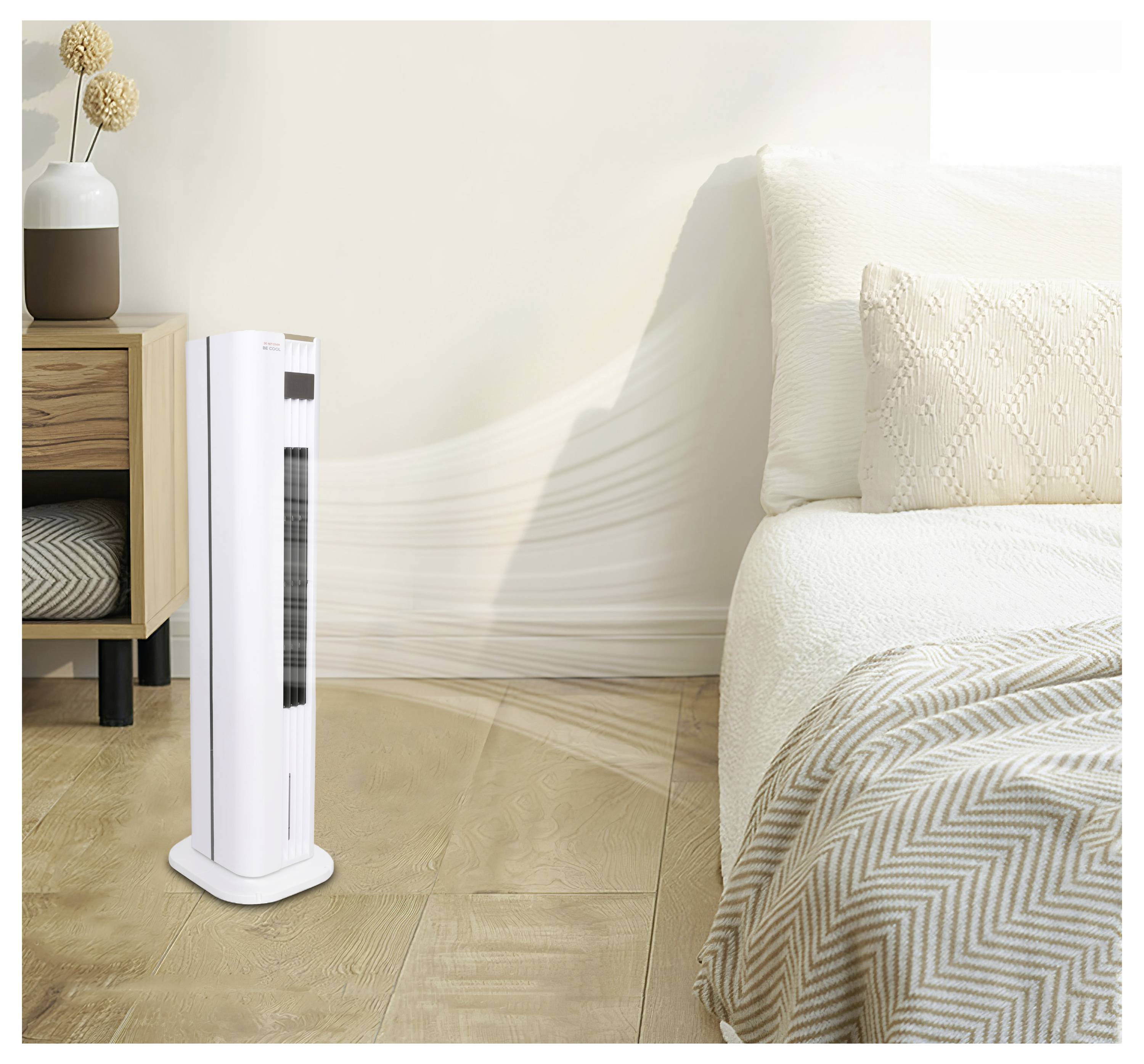 Ein weißer Turmventilator steht neben einem modernen Bett mit weißer und gemusterter Bettwäsche in einem sanft beleuchteten Zimmer. Ein hölzerner Nachttisch mit Vasen befindet sich in der Nähe.