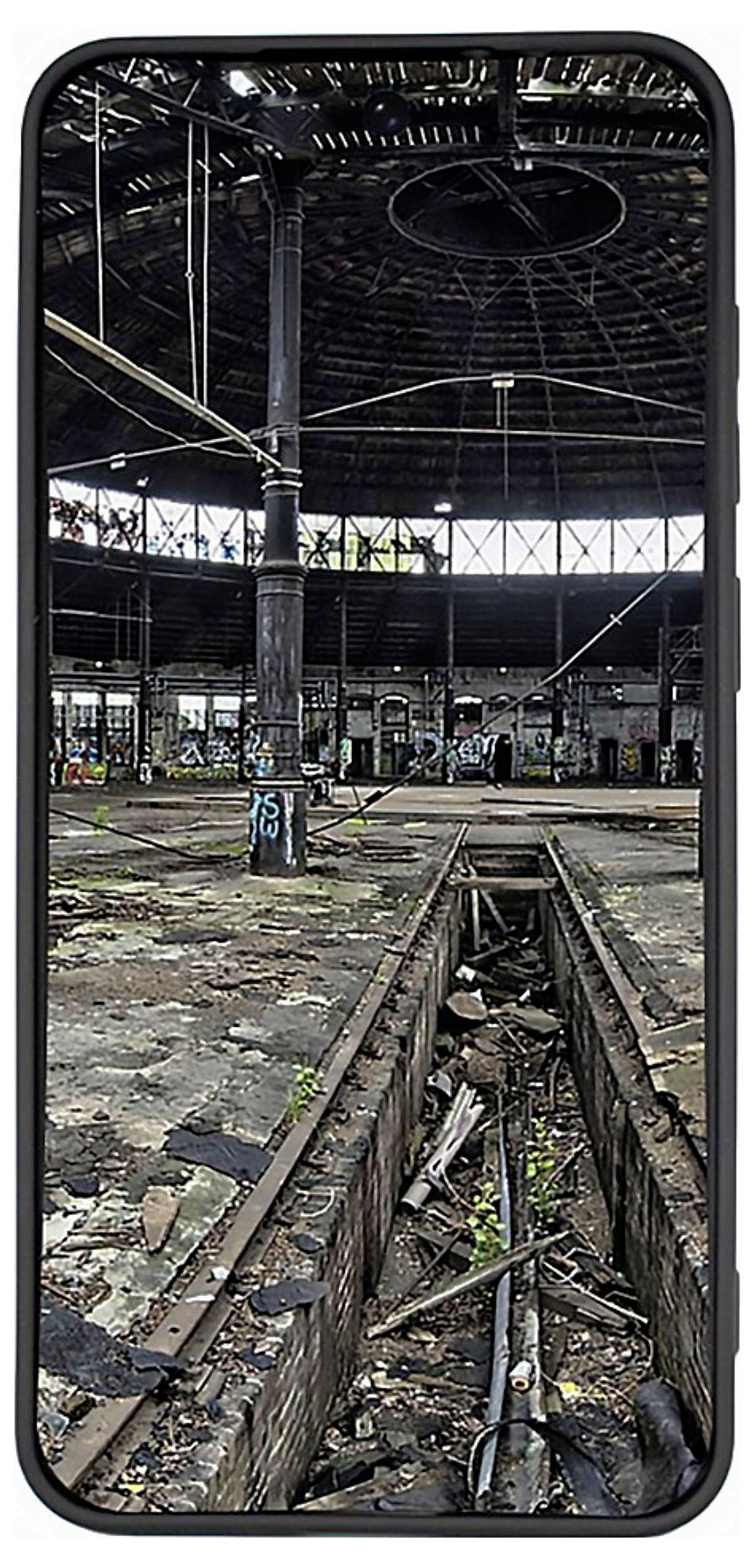 „Verlassenes Industriegebäude mit Graffiti an den Wänden, zerbrochenen Fenstern und überwucherter Vegetation, dargestellt auf einem Smartphone-Bildschirm."