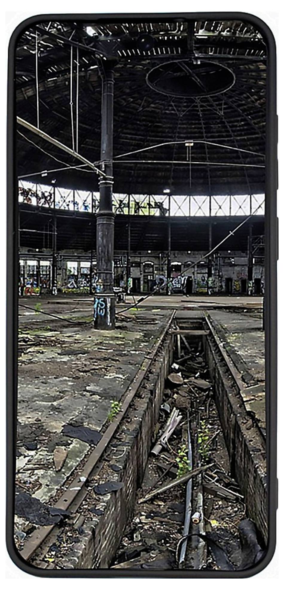 Ein altes Bahnhofsgebäude, das durch einen Smartphone-Bildschirm zu sehen ist. Das Innere ist verlassen, mit beschädigtem Boden und Graffiti an den Wänden.