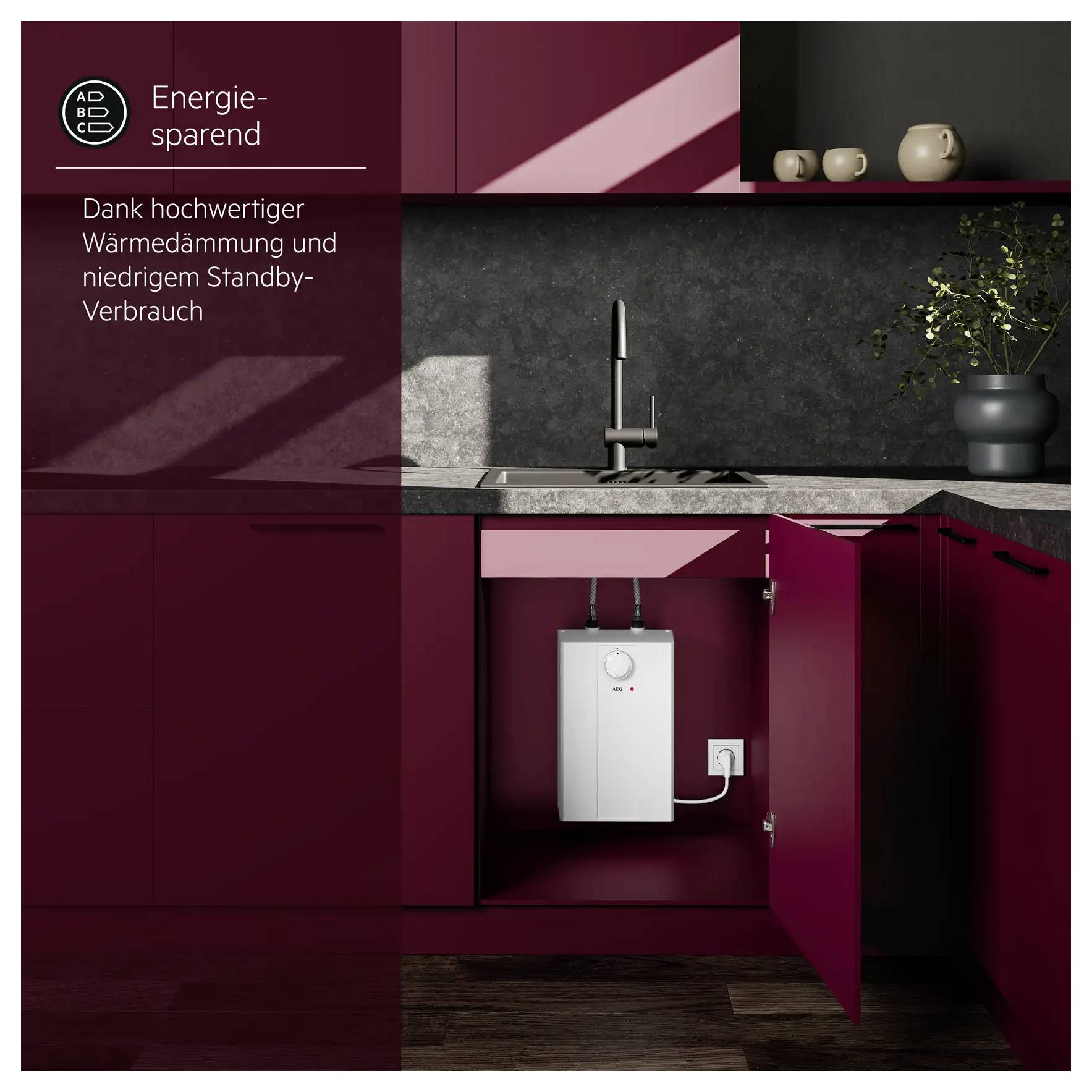 Eine moderne Küche mit roter Schrankwerk zeigt einen offenen Schrank unter dem Waschbecken, in dem ein energiesparender Warmwasserspeicher sichtbar ist. Der Text hebt die Energieeffizienz hervor.