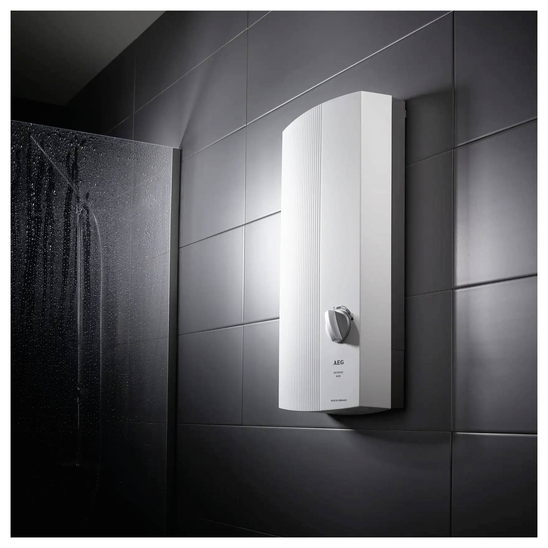 Ein moderner Elektroboiler aus Weiß an einer gekachelten dunklen Badezimmerwand neben einer Dusche montiert.