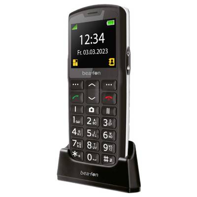 Ein schwarzes Mobiltelefon mit großen Tasten, einem kleinen Display, das '12:34' anzeigt, und dem Datum 'Fr. 03.03.2023', auf einer Ladestation platziert.
