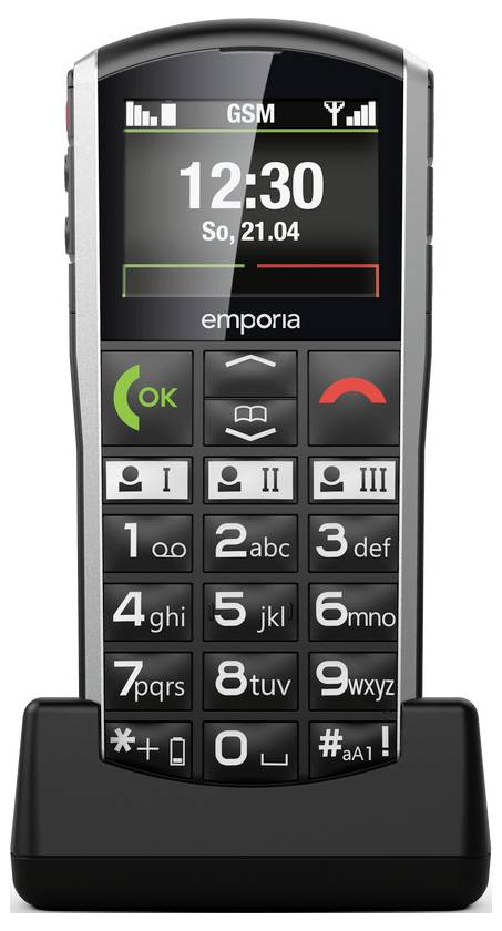 Ein Mobiltelefon mit großen Tasten, einem Bildschirm mit der Anzeige „12:30", Batteriestatusanzeige und GSM-Signalindikatoren, in einer Ladestation.