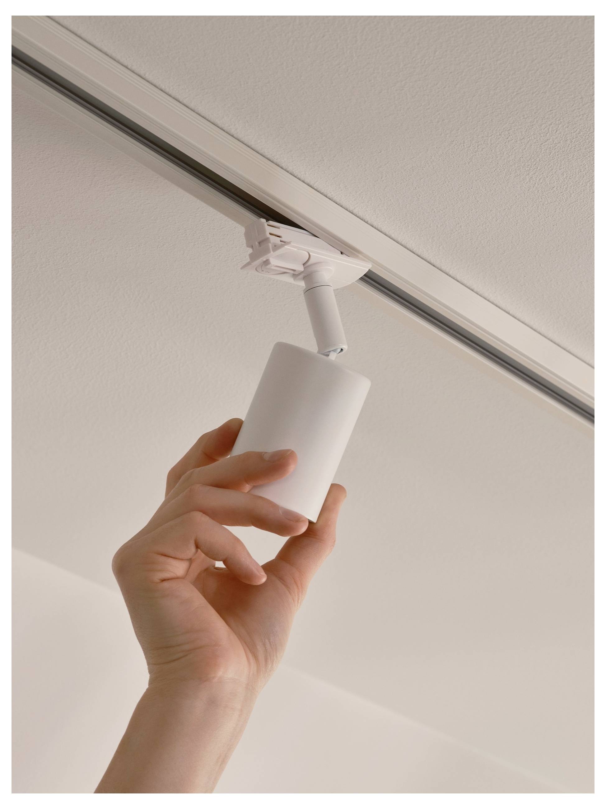 Eine Person montiert eine zylindrische Leuchte an einer Deckenleiste mit einer Hand und zeigt dabei eine einfache und elegante Methode zur Beleuchtungsinstallation im Haus.