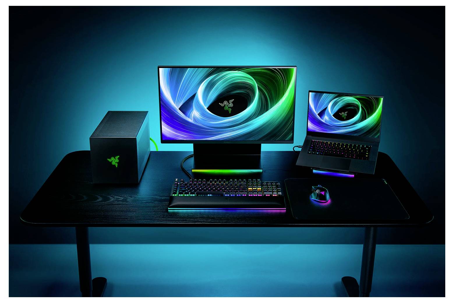 Ein modernes Gaming-Setup mit einem Desktop-Computer, Monitor und Laptop auf einem Schreibtisch, beleuchtet durch farbige LED-Lichter.