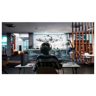Eine Person mit Kopfhörern programmiert in einem modernen Büro, konzentriert auf mehrere Monitore, auf denen Code angezeigt wird, mit einem großen Flugzeugmural im Hintergrund.