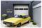 Ein gelbes Vintage-Auto ist auf einer Ziegelestein-Einfahrt vor einer modernen Garage geparkt, mit zwei an der Wand montierten Schildern, die Temperatur und Geschlossenheit anzeigen.