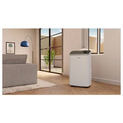 Tragbarer weißer Luftreiniger/Entfeuchter in einem modernen Wohnzimmer neben einem Sofa, einer Stehlampe und Fenstern mit Holzjalousien.